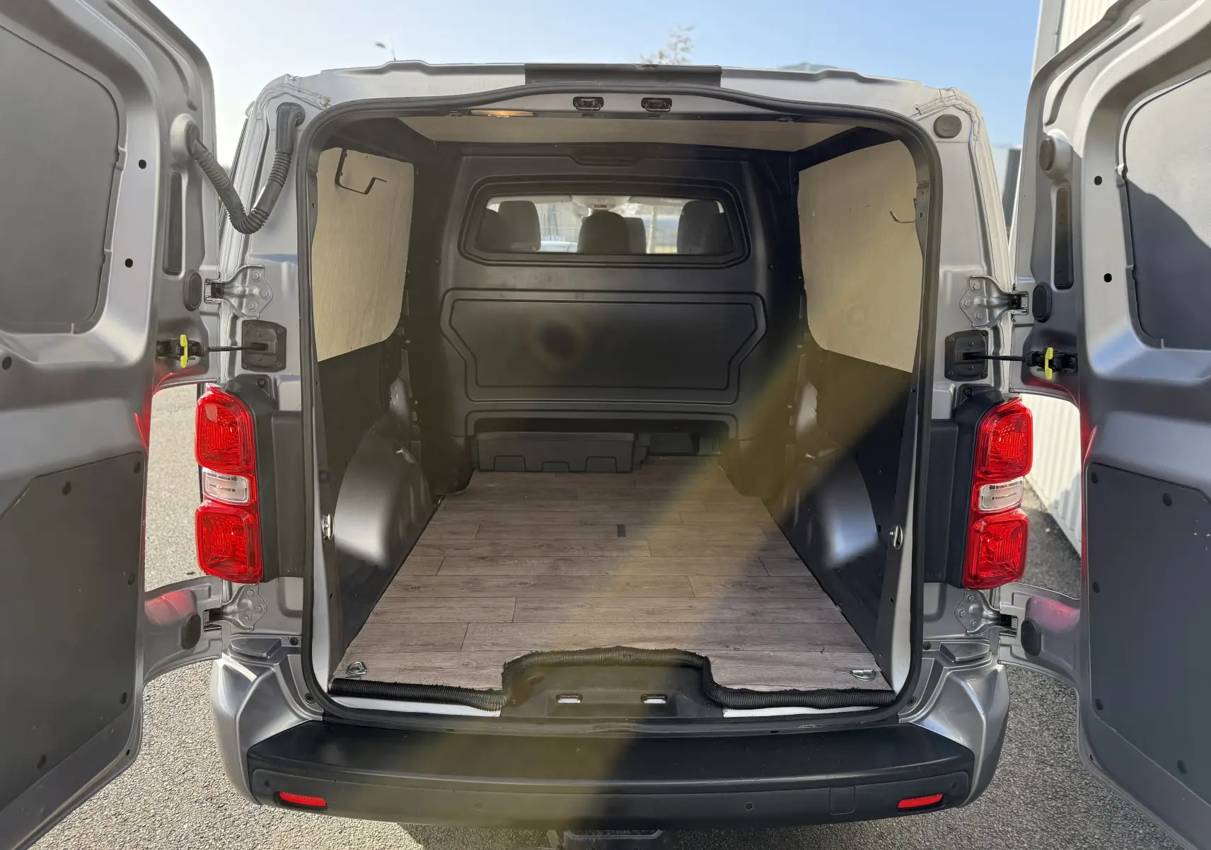 Vue arrière du FIAT Scudo cabine approfondie gris 2022, portes ouvertes dévoilant un espace de chargement vide avec plancher imitation bois.