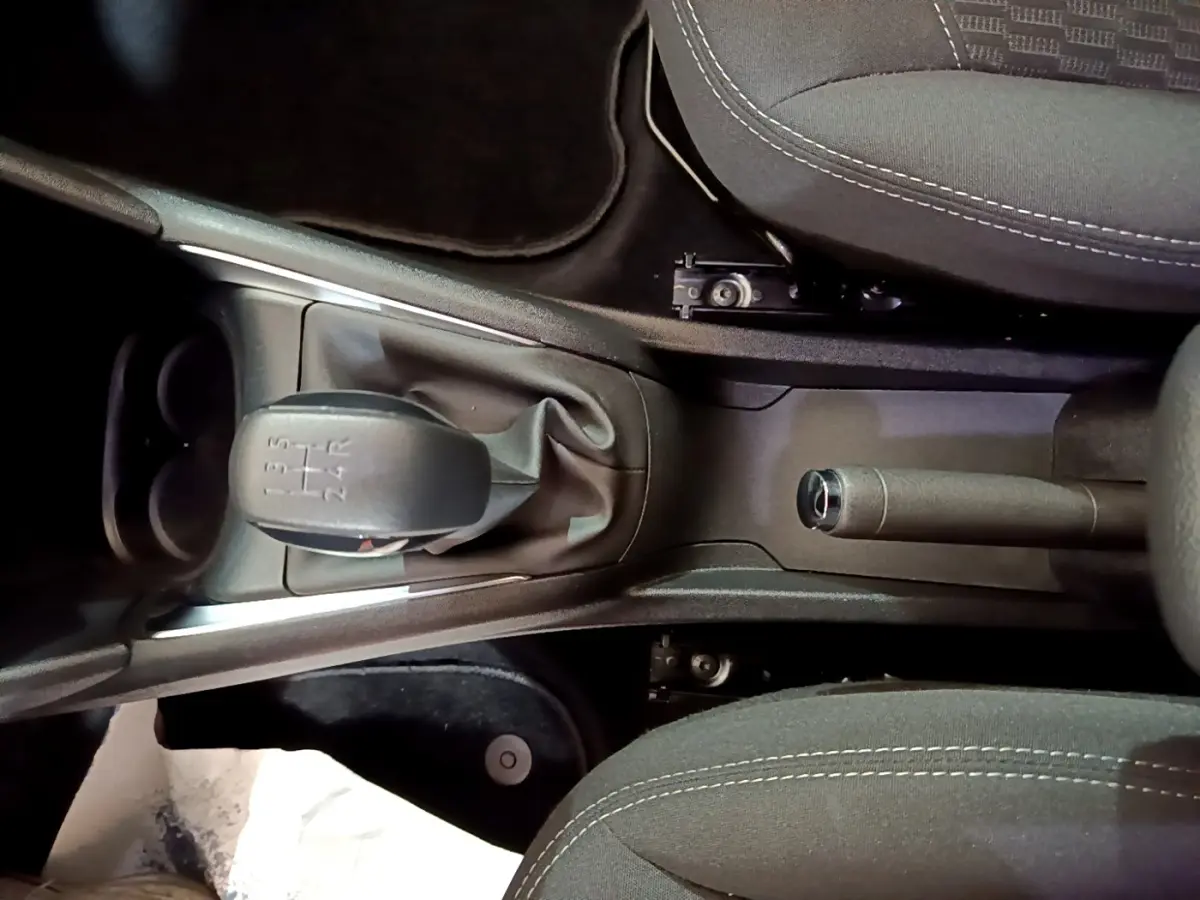 Vue plongeante sur la console centrale noire de la Peugeot 208 blanche, avec levier de vitesse manuel et frein à main.