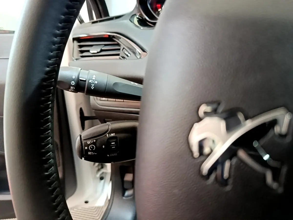 Gros plan sur le volant noir avec logo Peugeot et commandes au volant, intérieur de la Peugeot 208 blanche 2018.