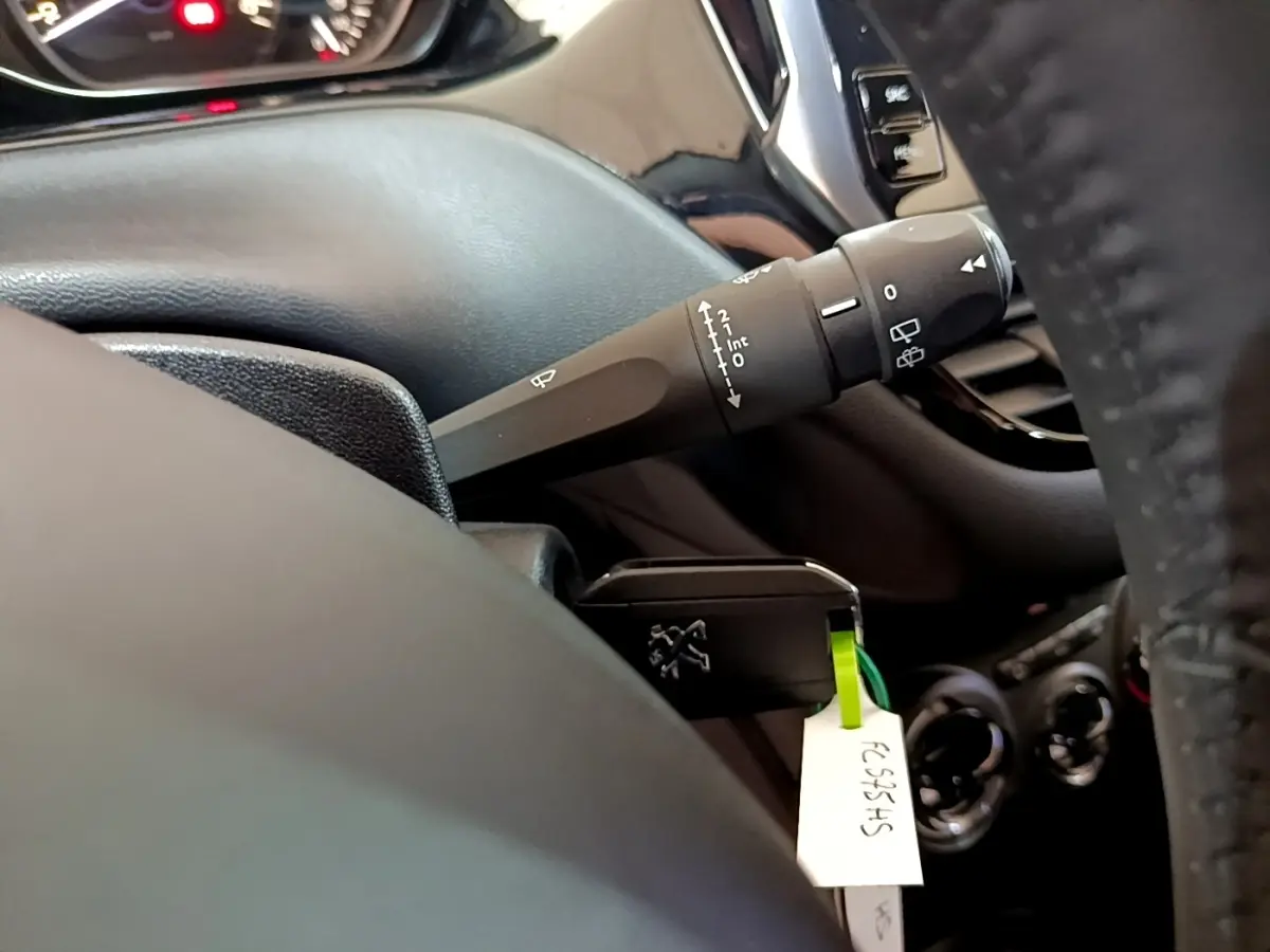 Détail intérieur du Peugeot 208 blanc de 2018 montrant la manette d’essuie-glace côté gauche et partie du tableau de bord.