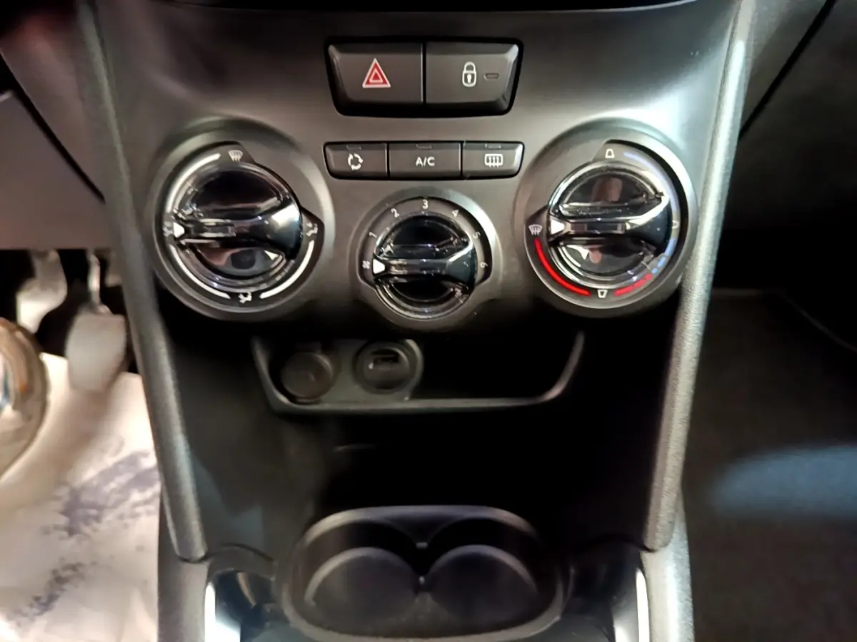 Vue rapprochée des commandes de climatisation et des boutons centraux du tableau de bord d’une Peugeot 208 blanche.