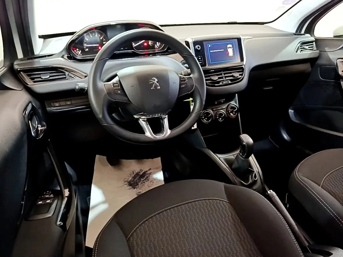 Intérieur noir Peugeot 208 Puretech 82, vue du poste de conduite avec volant, écran tactile et boîte manuelle.