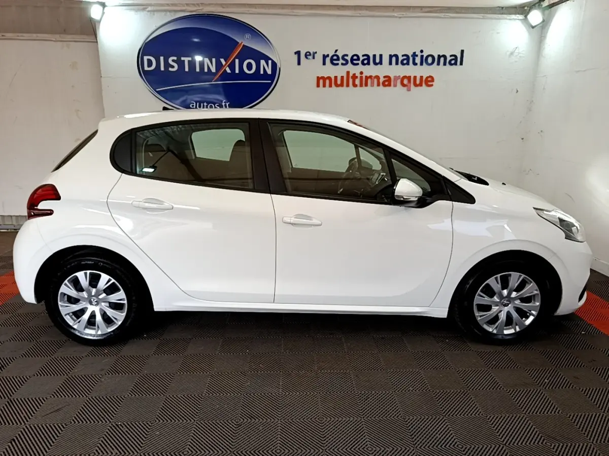 Profil côté droit d'une Peugeot 208 blanche Puretech 82 S&S ACTIVE BUSINESS, en intérieur sur sol damier noir et rouge.