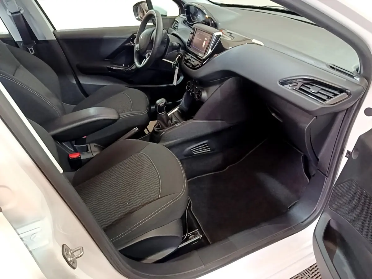 Intérieur côté passager d’une Peugeot 208 blanche, montrant les sièges noirs et le tableau de bord avec écran tactile.