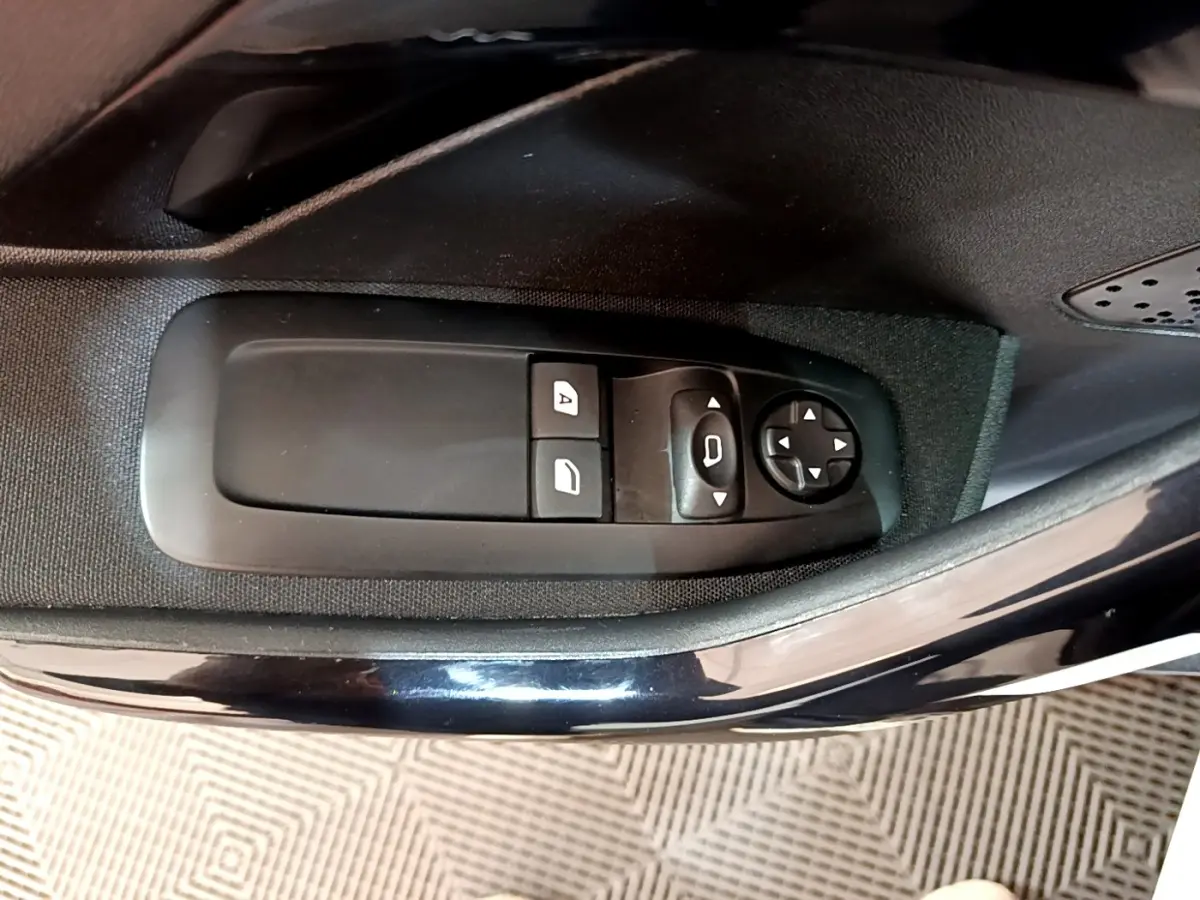Gros plan sur les commandes de réglage des rétroviseurs et des vitres côté conducteur d’une Peugeot 208 blanche.