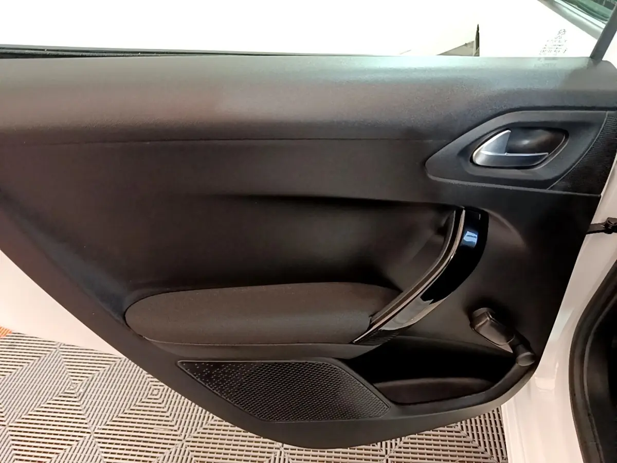 Vue intérieure de la porte avant droite noire avec poignée chromée d'une Peugeot 208 blanche de 2018.