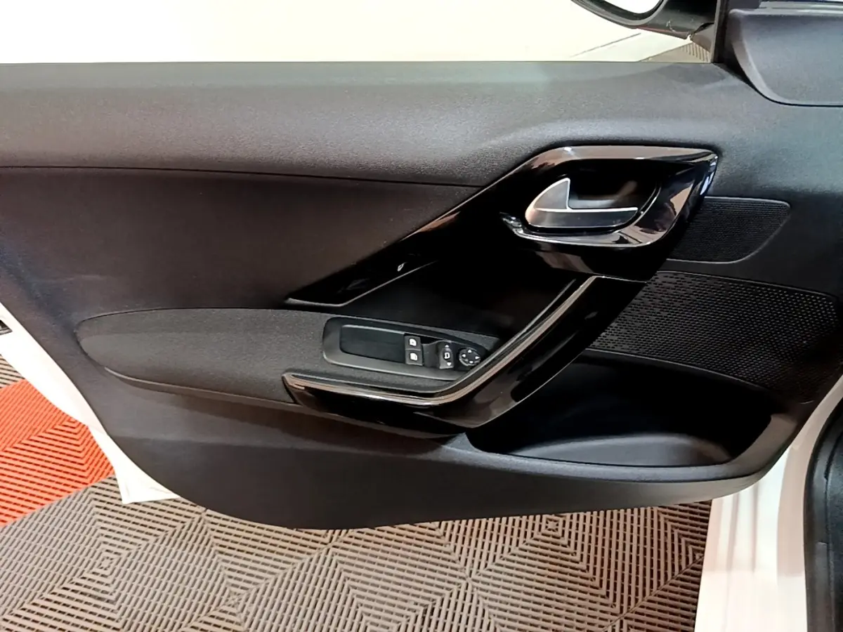 Vue rapprochée de la porte intérieure côté conducteur d’une Peugeot 208 blanche, avec poignée et commandes électriques.