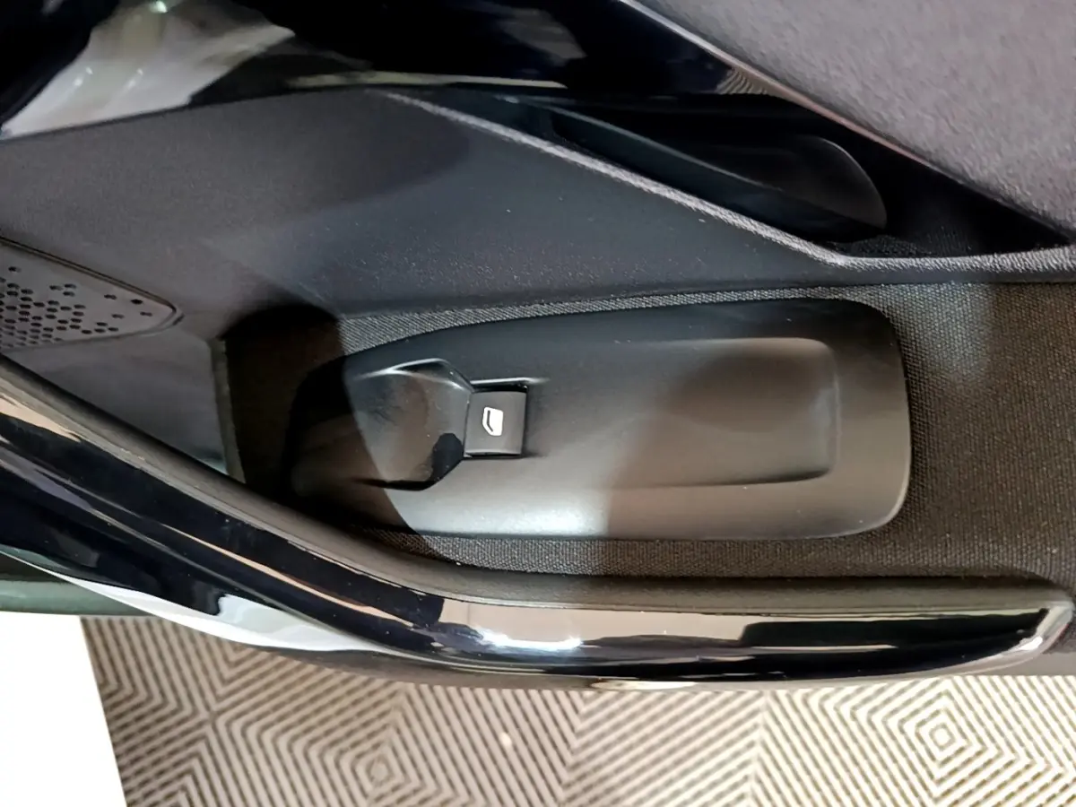 Gros plan sur le bouton d’ouverture de coffre côté intérieur d’une Peugeot 208 blanche, détail de la portière.