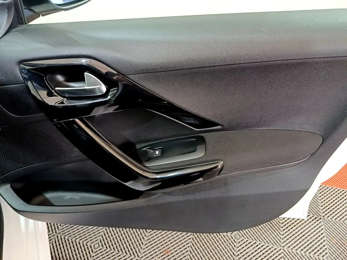 Vue rapprochée de la porte intérieure côté gauche d’une Peugeot 208 blanche, avec poignée noire brillante.