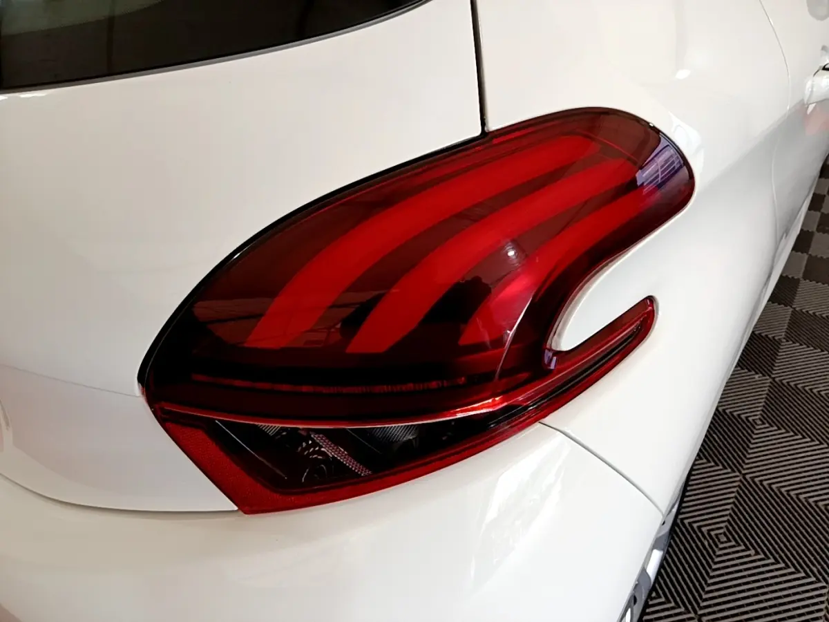 Gros plan sur le feu arrière droit rouge d’une Peugeot 208 blanche vue de l’arrière côté droit.