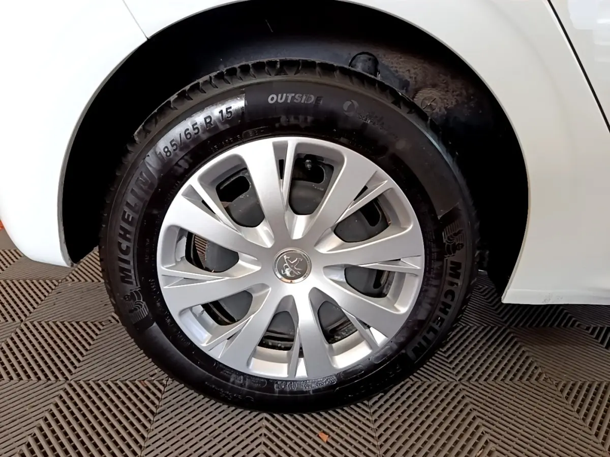 Gros plan sur la roue avant droite d'une Peugeot 208 blanche, avec jante argentée et pneu Michelin visible.