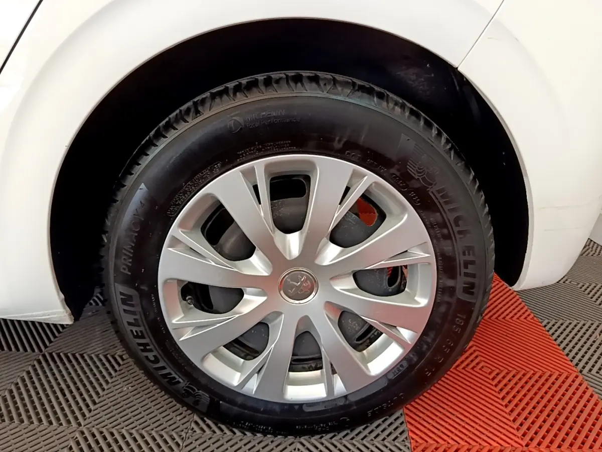 Gros plan sur la roue avant gauche d'une Peugeot 208 blanche, avec jante argentée et pneu Michelin.