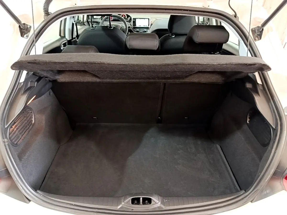 Vue arrière du coffre ouvert d'une Peugeot 208 blanche, montrant l'espace de chargement et la tablette arrière relevée.