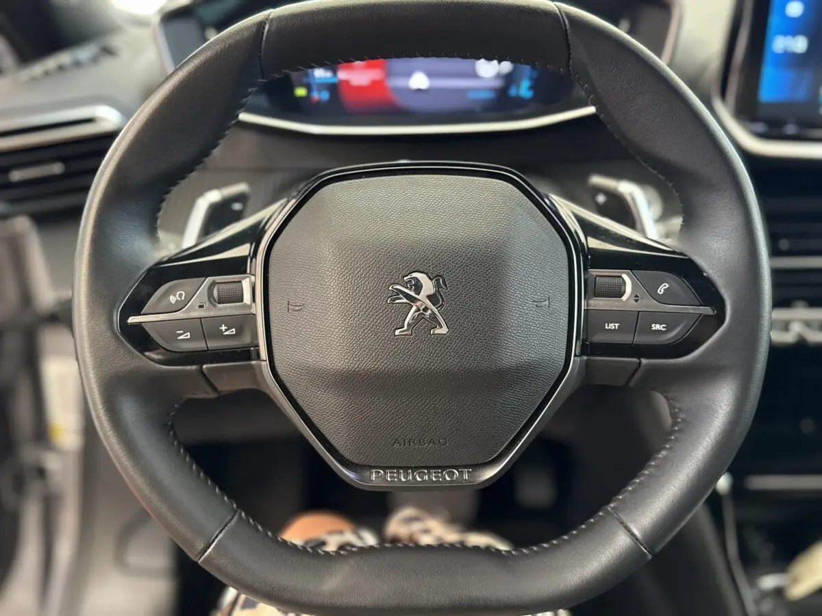 Gros plan sur le volant cuir noir du Peugeot 2008 2023 avec commandes intégrées et logo lion central.