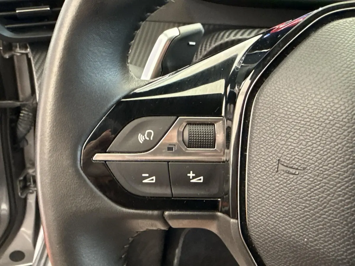 Gros plan sur les commandes gauche du volant cuir noir du Peugeot 2008 gris clair, version PureTech 130 S&S EAT8 Allure 2023.