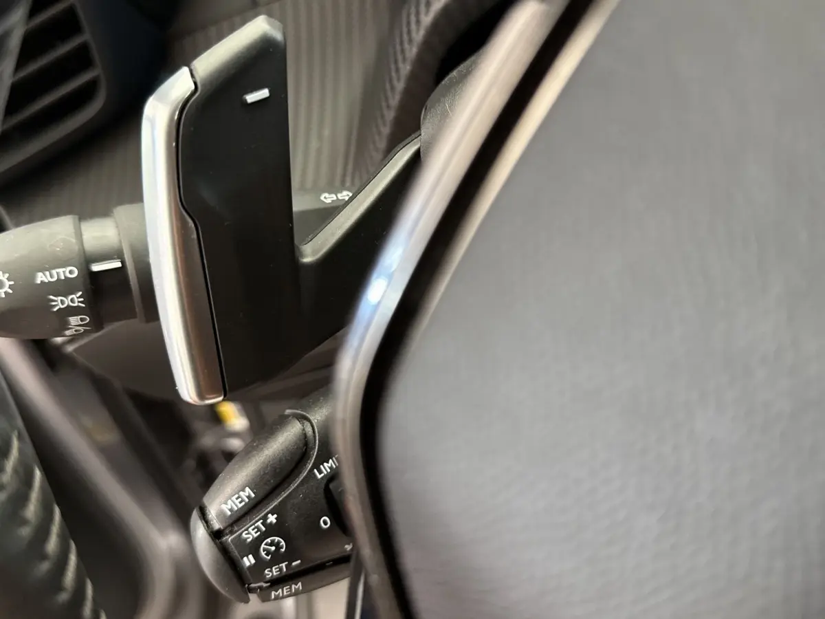 Détail du volant cuir de la Peugeot 2008 gris clair, avec commandes de régulateur de vitesse et leviers multifonctions.