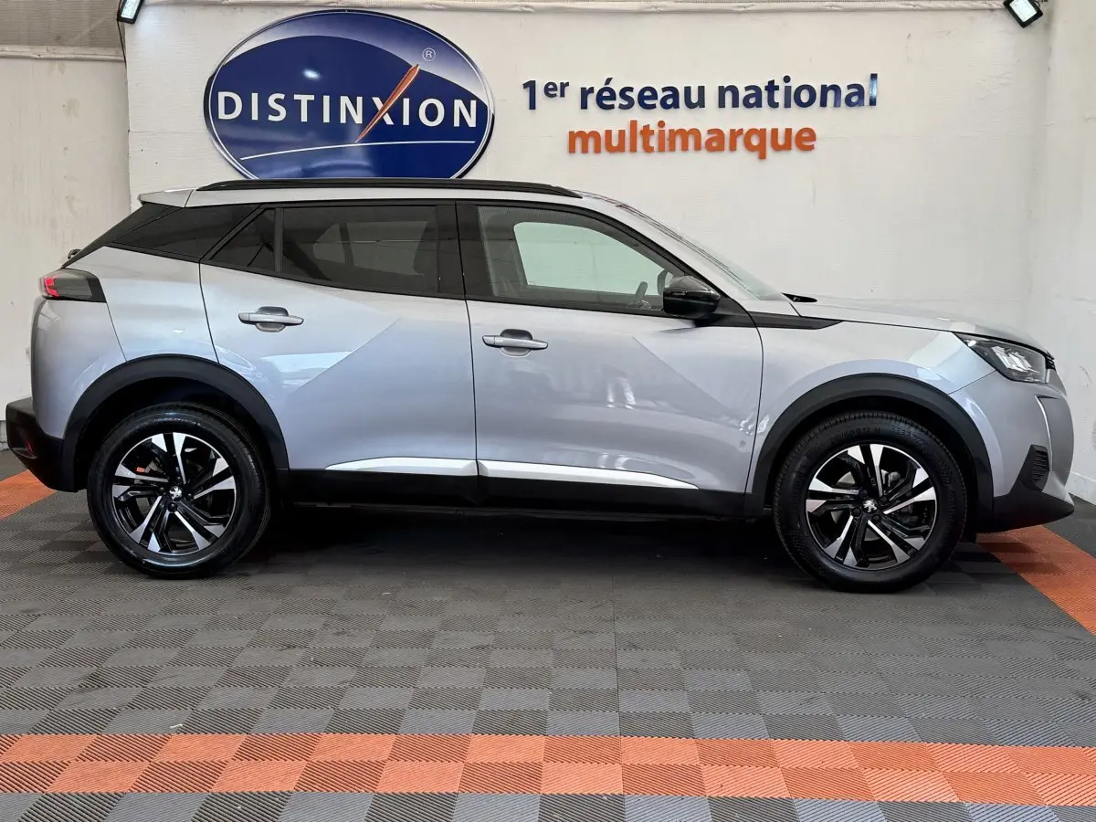 Profil droit du Peugeot 2008 gris clair 2023 avec jantes noires et toit noir contrasté, stationné en intérieur showroom.