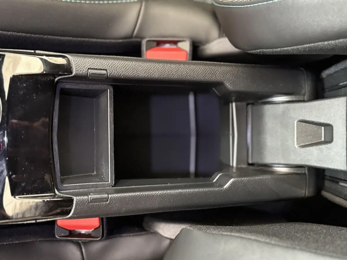 Vue plongeante sur la console centrale noire du Peugeot 2008 gris clair, avec rangement ouvert entre les sièges avant.