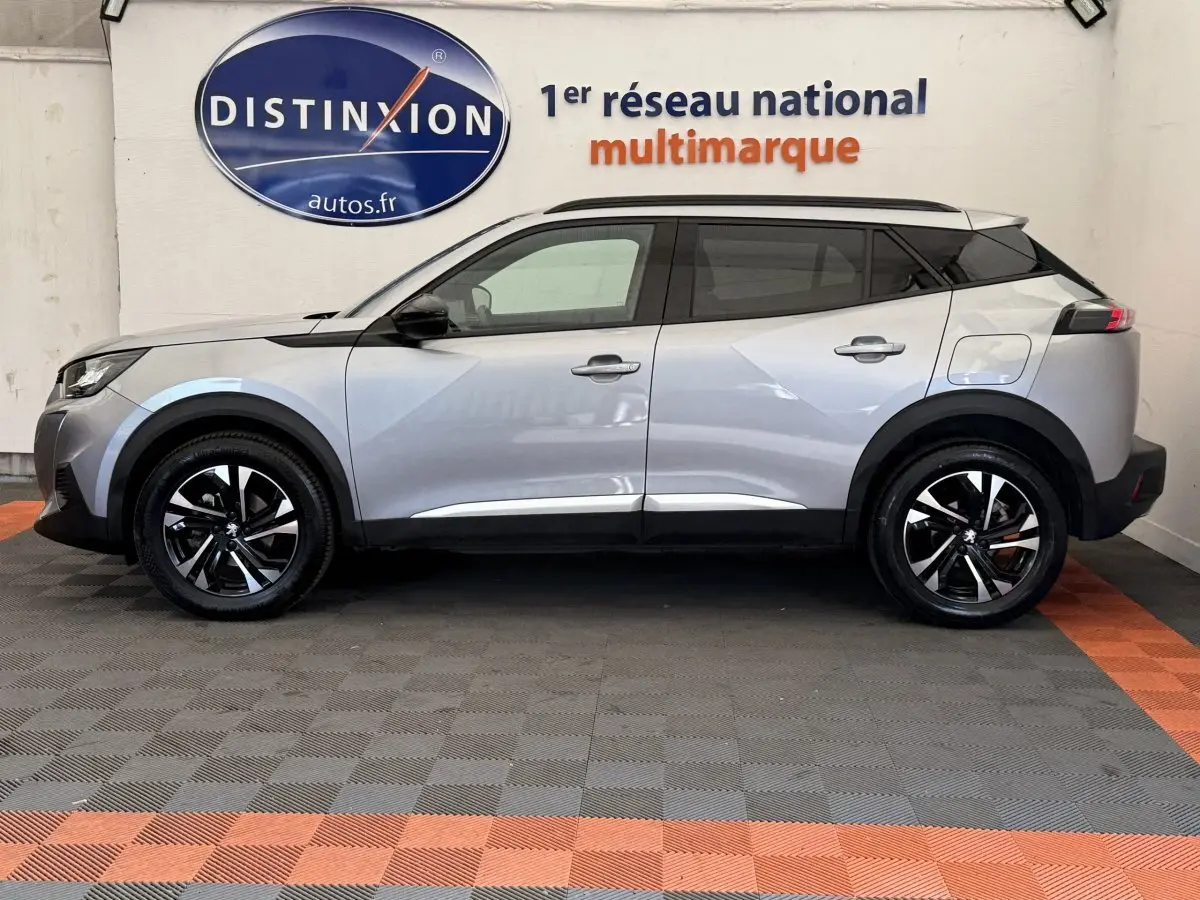 Profil côté gauche d'un Peugeot 2008 gris clair 2023, avec jantes noires et toit noir contrastant, en intérieur showroom.