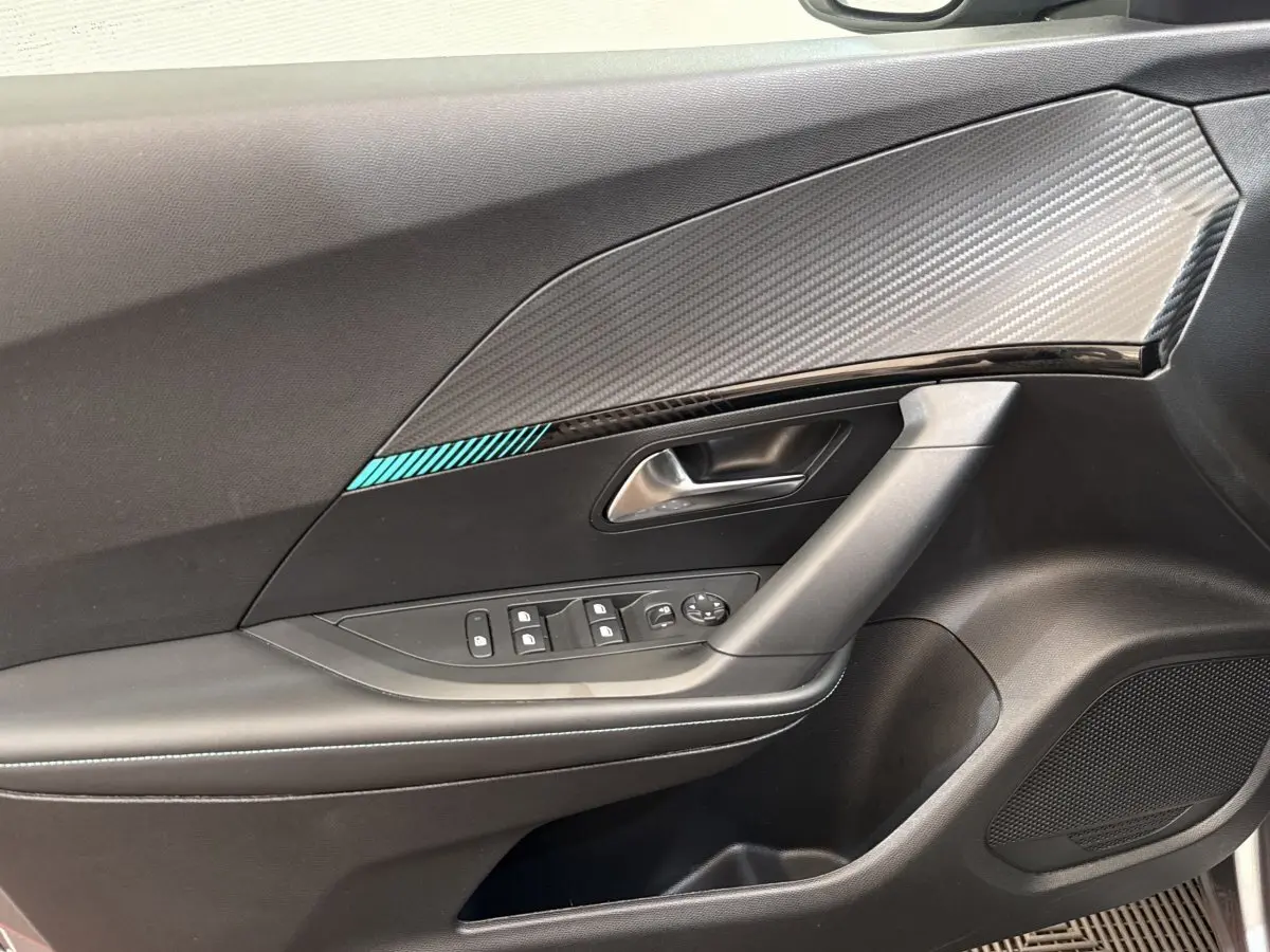 Vue rapprochée de la porte côté conducteur d’une Peugeot 2008 gris clair, avec insert décor carbone et commandes électriques.