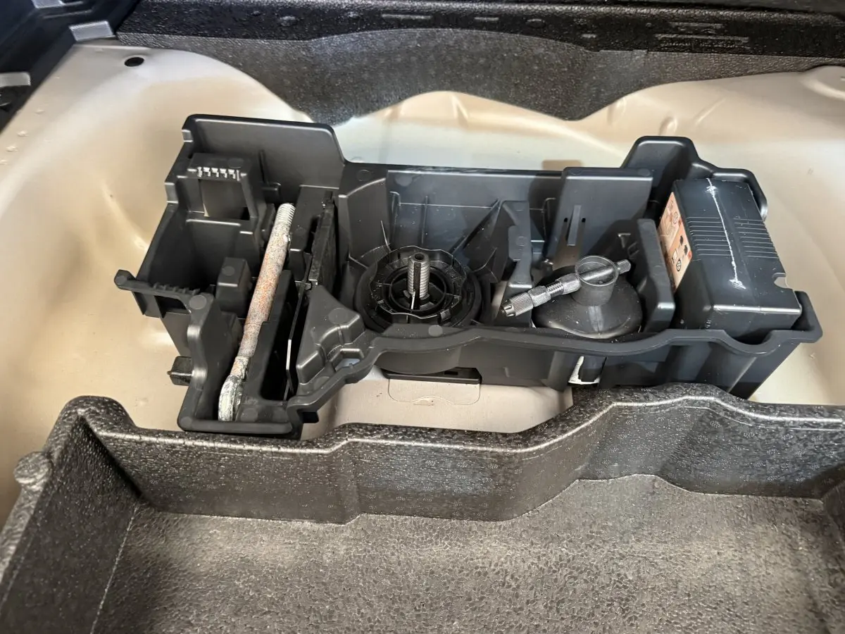 Gros plan sur le rangement d'outils dans le coffre beige d'un Peugeot 2008 gris clair, sans vue extérieure du véhicule.