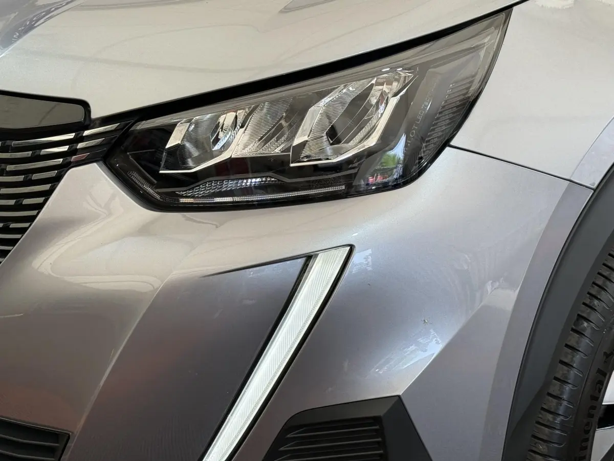 Gros plan sur le phare avant droit et la calandre d’un Peugeot 2008 gris clair avec feux LED distinctifs.