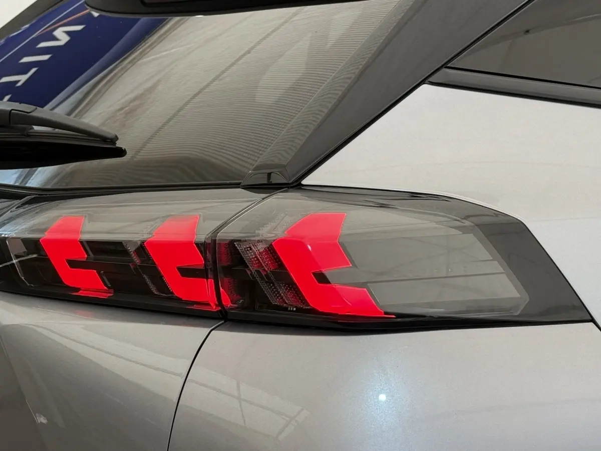 Gros plan sur le feu arrière droit rouge vif du Peugeot 2008 gris clair, soulignant le design moderne du SUV.