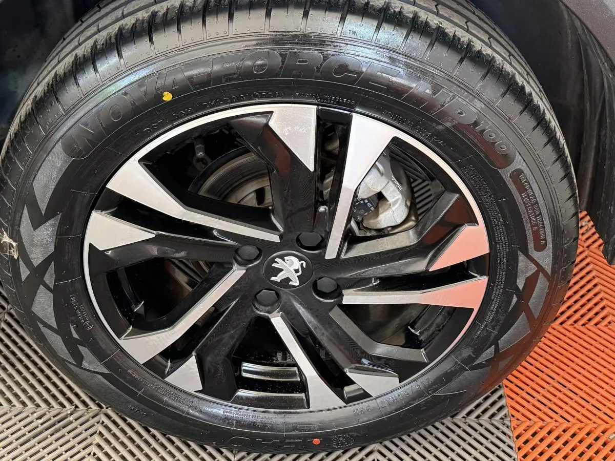 Vue rapprochée sur la roue avant droite d'un Peugeot 2008 gris clair, soulignant le pneu et la jante noire.