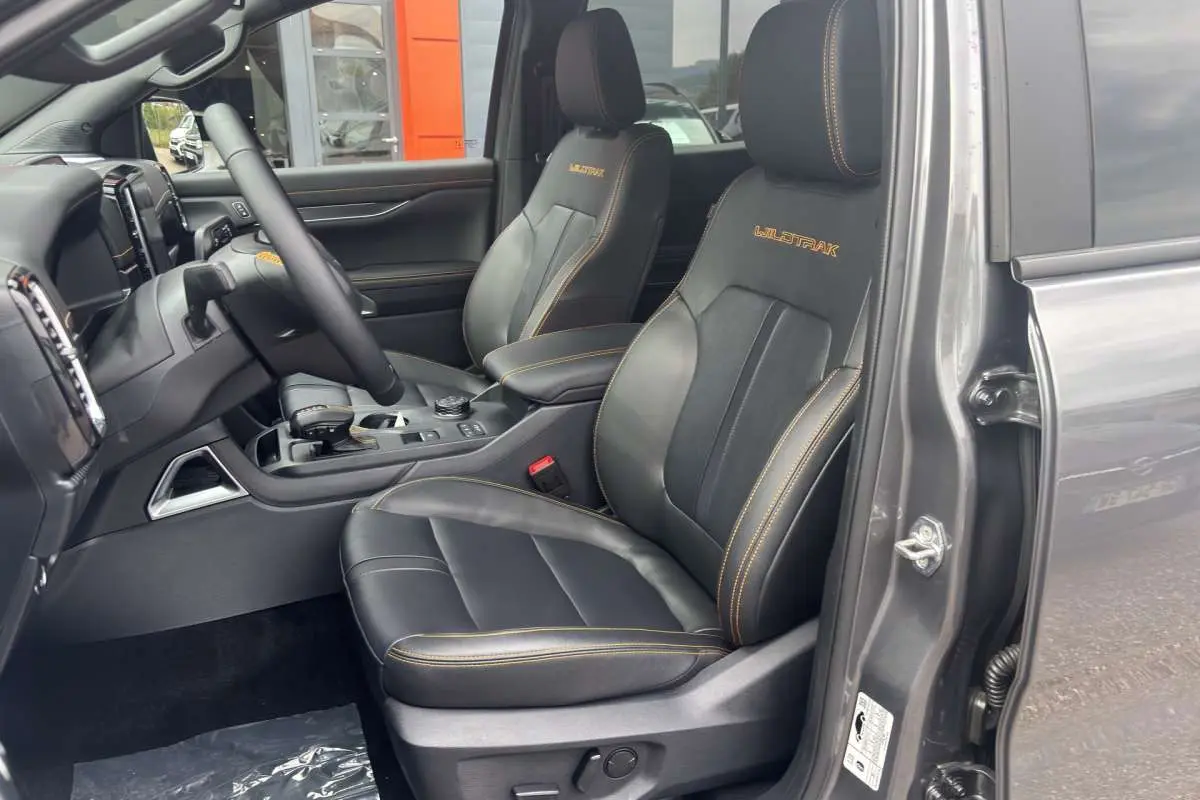 Vue intérieure côté conducteur du Ford Ranger Wildtrak 2026 gris carbone, sièges cuir noirs avec surpiqûres orange et logo Wildtrak brodé.