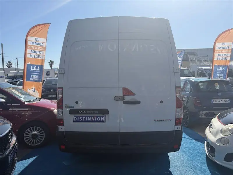 Vue arrière d’un Renault Master blanc stationné en extérieur, avec panneaux publicitaires orange visibles de chaque côté.