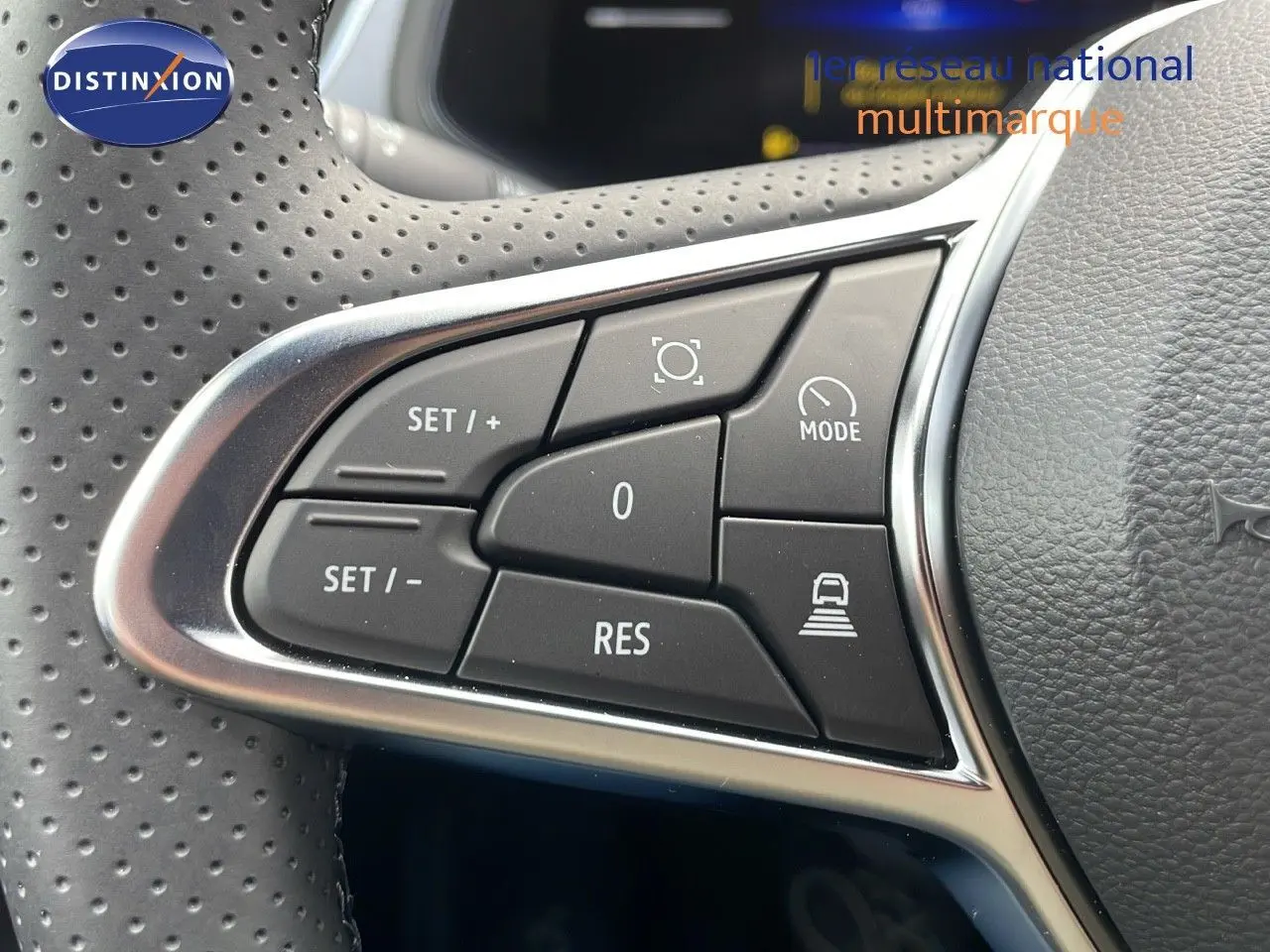 Gros plan sur les commandes de régulateur de vitesse au volant perforé d'un Renault Captur E-Tech hybride rouge 2025.