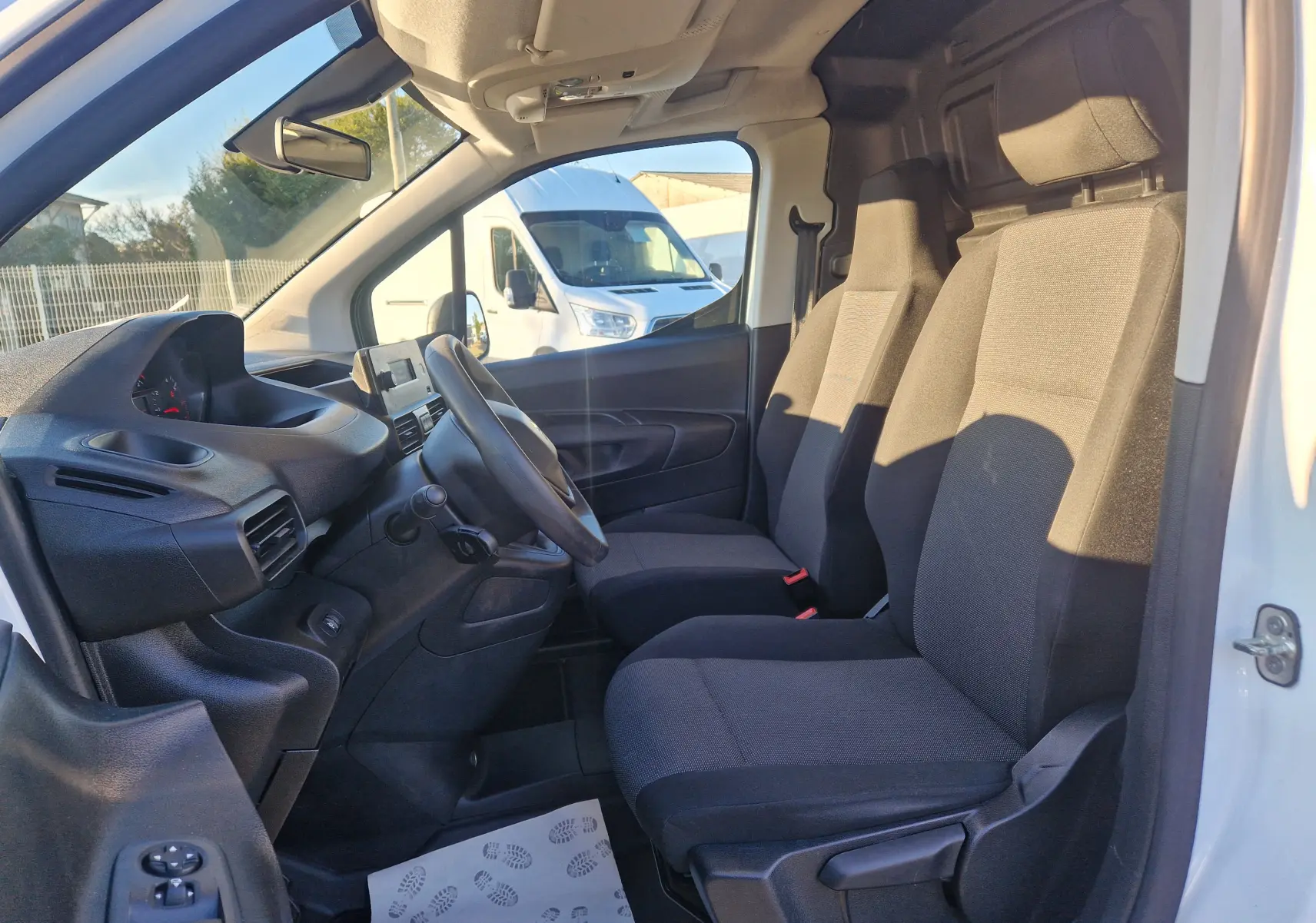 Vue intérieure côté gauche du Peugeot Partner blanc 2021, montrant les sièges avant et le tableau de bord simple.