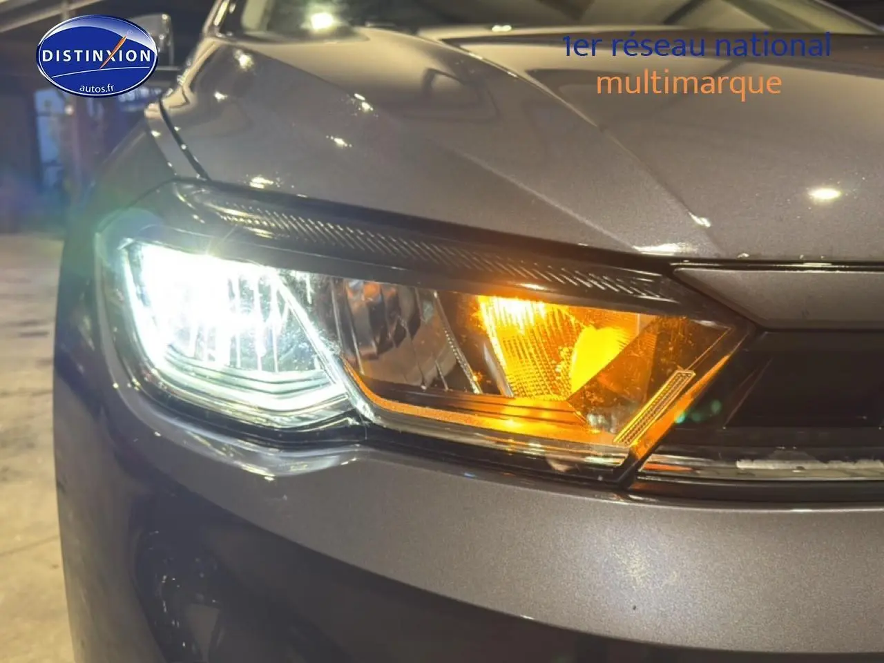 Gros plan sur le phare avant gauche allumé d'une Volkswagen Polo gris cendre avec clignotant orange visible.