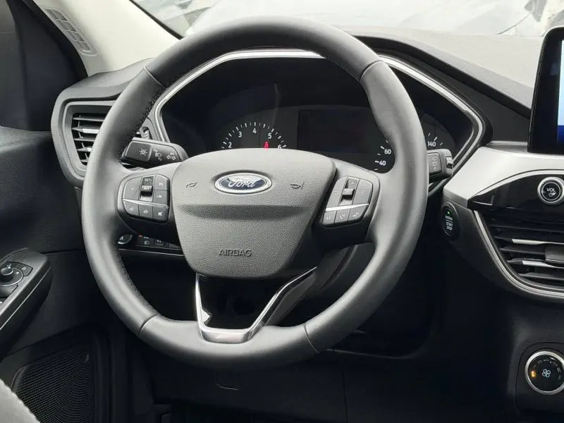 Vue intérieure centrée sur le volant noir du Ford Kuga 1.5 EcoBoost 2024, avec commandes intégrées et tableau de bord visible.