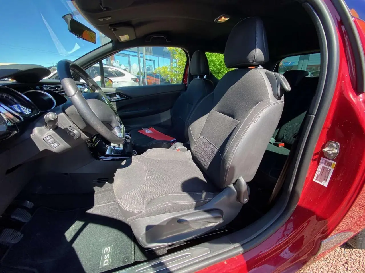 Vue intérieure côté conducteur d'une DS3 rouge avec sièges tissu gris et tableau de bord noir.