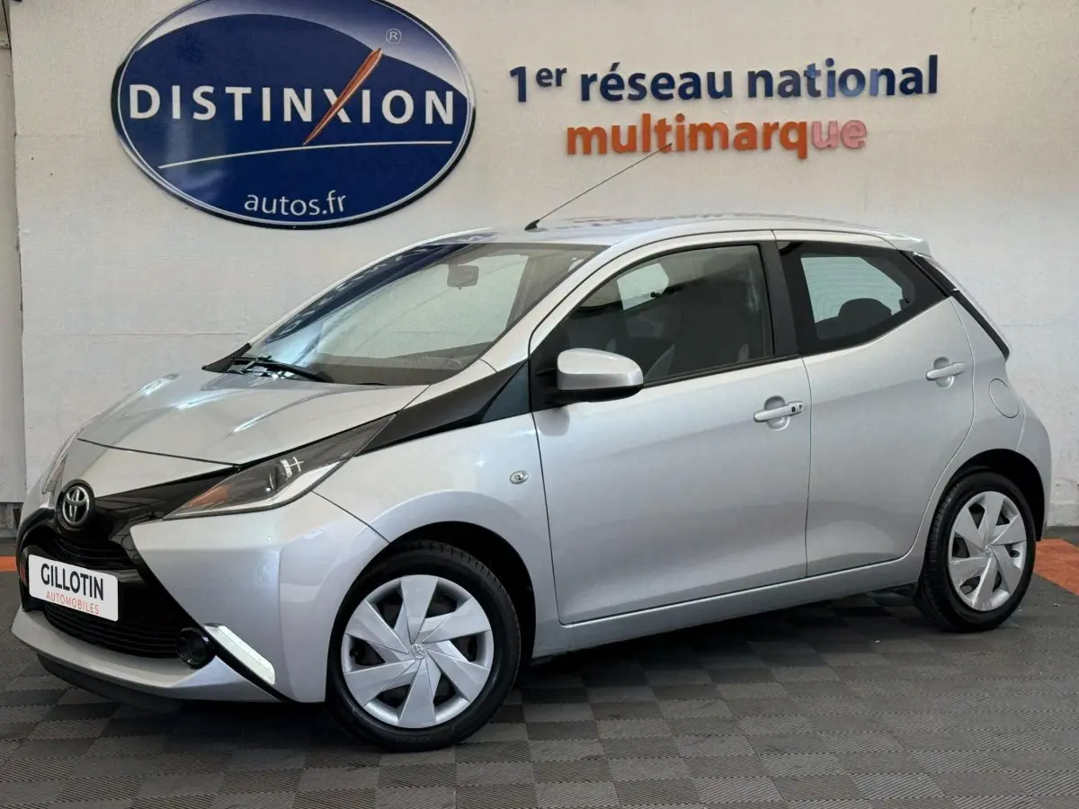 Toyota Aygo gris clair vue de profil côté gauche, soulignant son design compact et moderne en intérieur showroom.