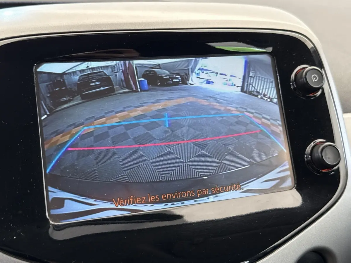 Vue de l'écran de caméra de recul d'une Toyota Aygo gris clair, affichant les lignes de guidage et l'arrière du véhicule.