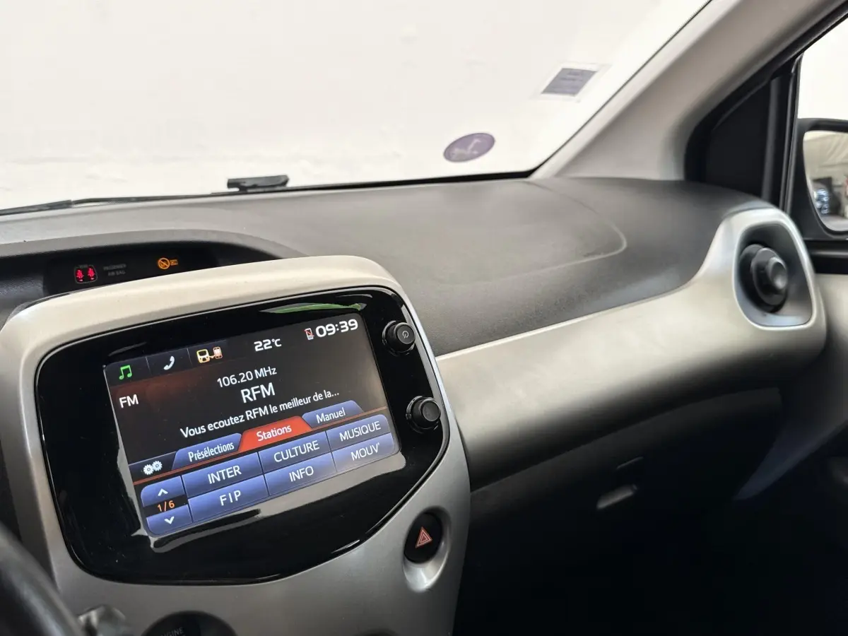 Vue intérieure du tableau de bord de la Toyota Aygo gris clair, avec écran tactile central affichant la radio FM.