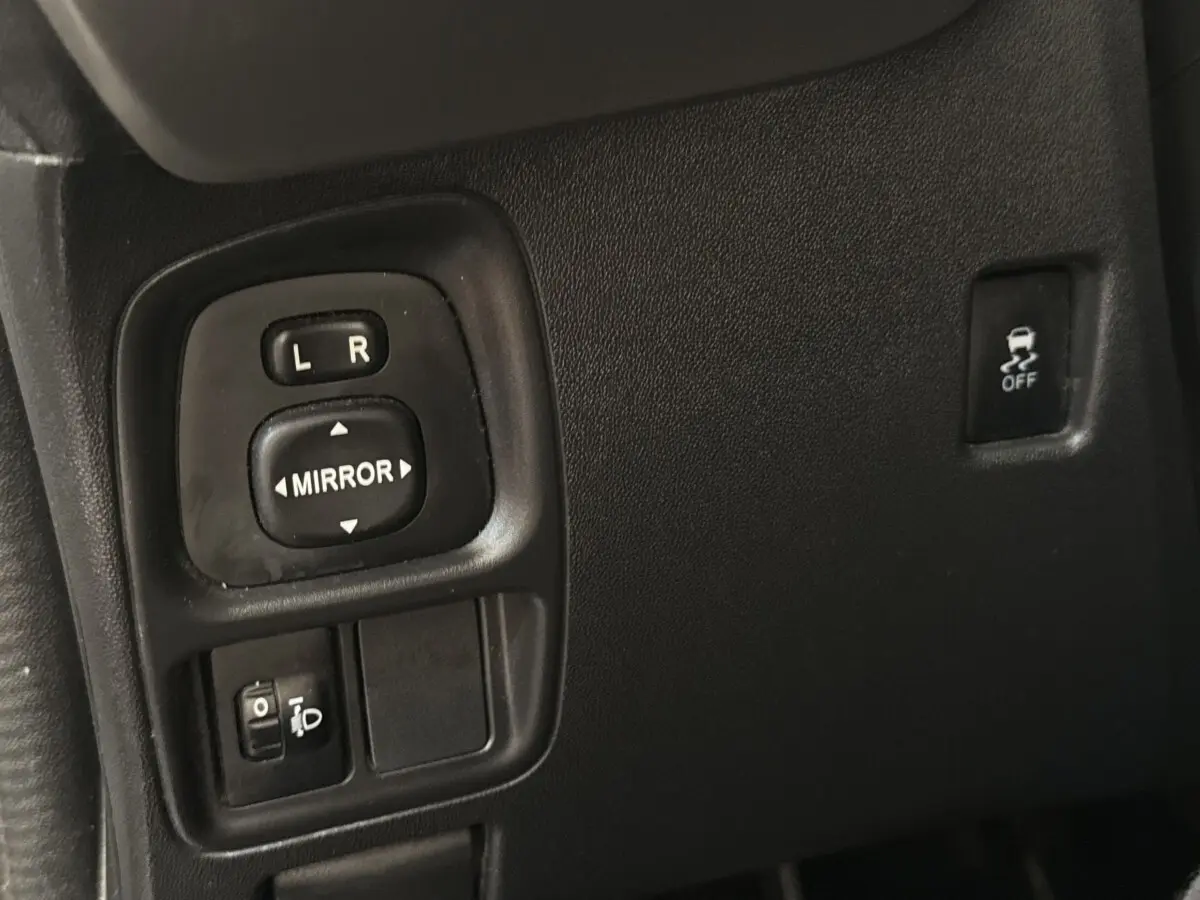 Gros plan sur les commandes de réglage des rétroviseurs et bouton antipatinage dans l'habitacle d'une Toyota Aygo gris clair.