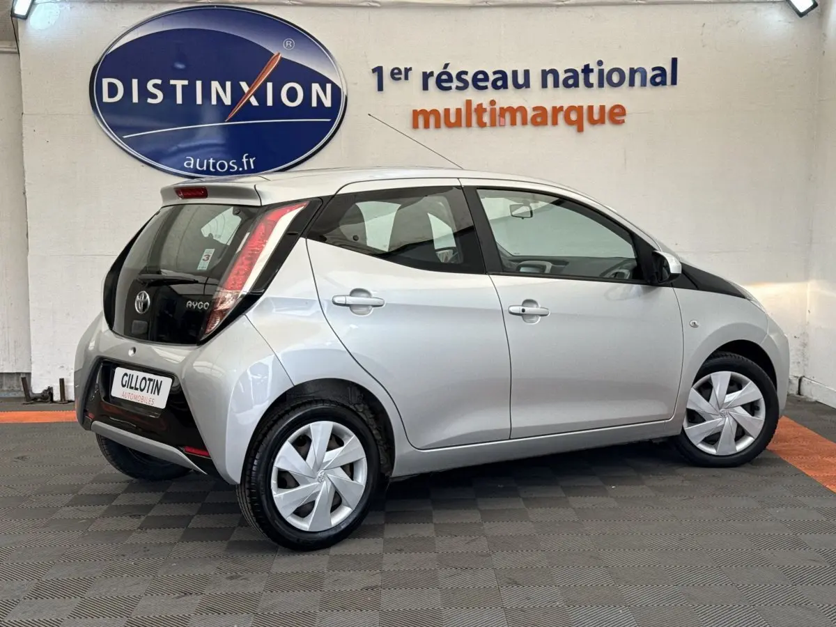 Vue 3/4 arrière droite d'une Toyota Aygo gris clair avec toit noir et feux arrière verticaux distinctifs.