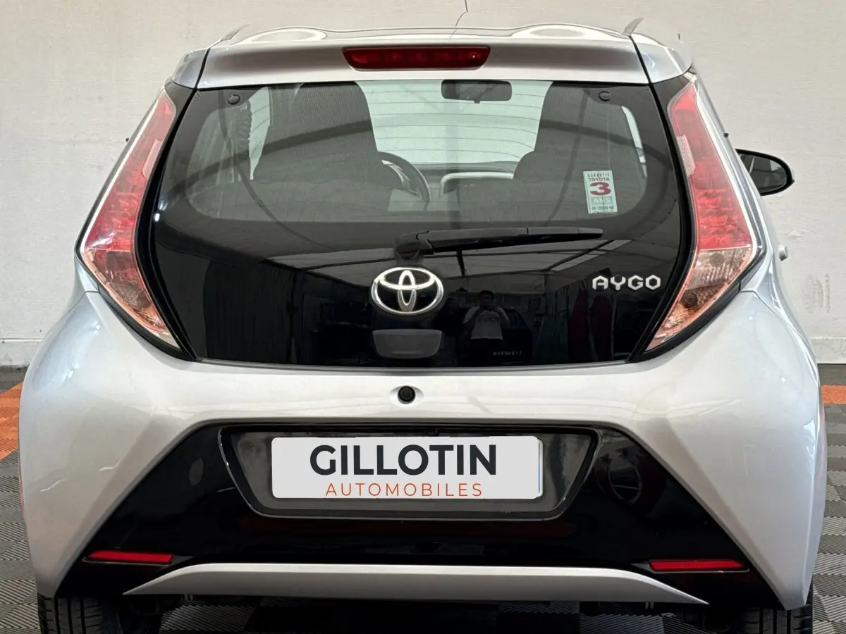 Vue arrière d'une Toyota Aygo gris clair avec hayon noir brillant et feux arrière verticaux distinctifs.