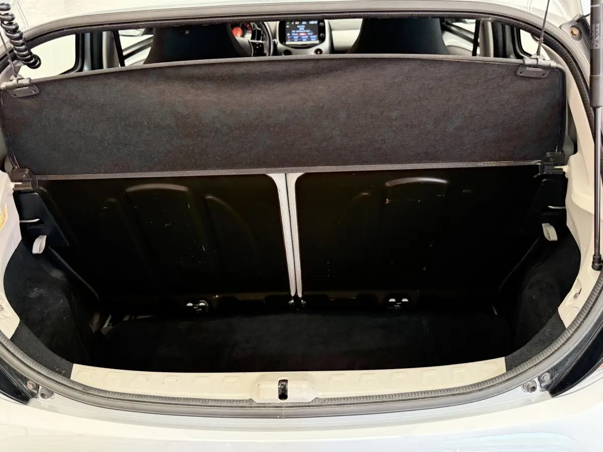 Vue du coffre arrière ouvert d'une Toyota Aygo gris clair, montrant la banquette rabattue et l'intérieur du coffre noir.