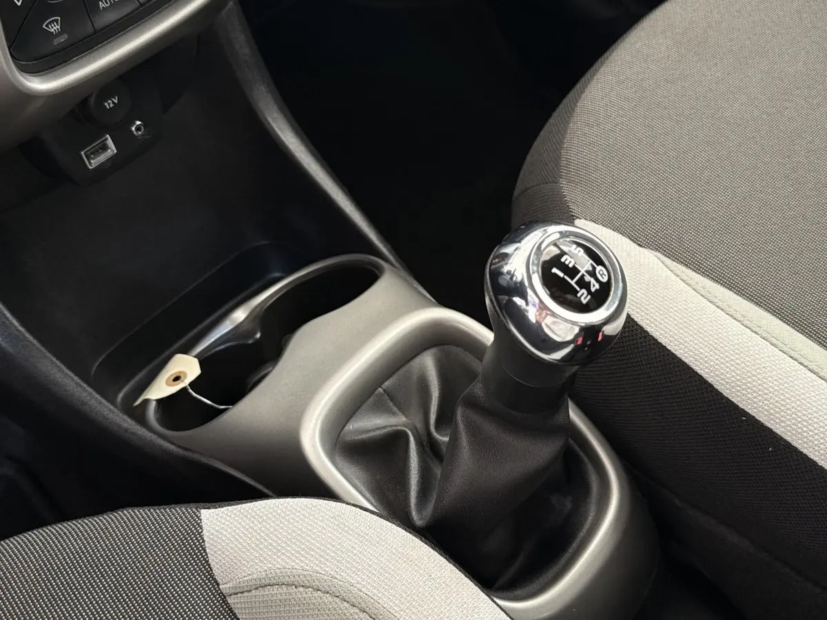 Gros plan sur le levier de vitesses manuel chromé et les sièges tissu gris clair et foncé d'une Toyota Aygo 2017.