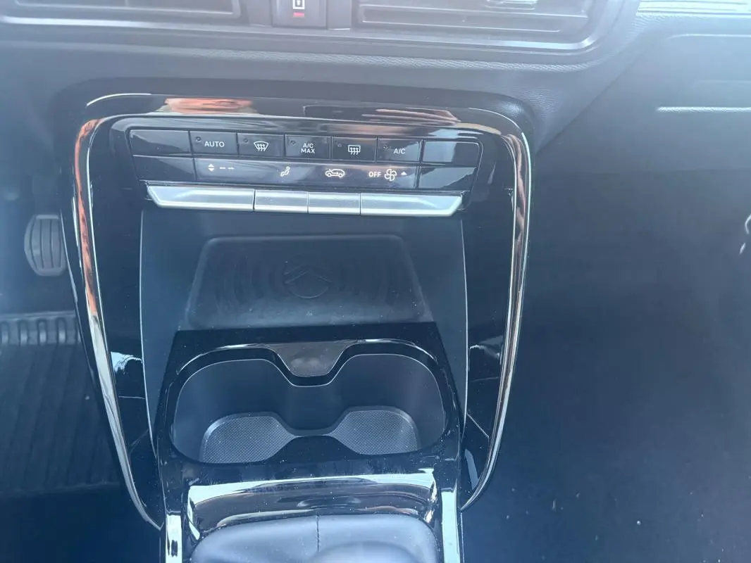 Vue rapprochée de la console centrale noire brillante du Citroën C3 2025, avec commandes climatisation et porte-gobelets.