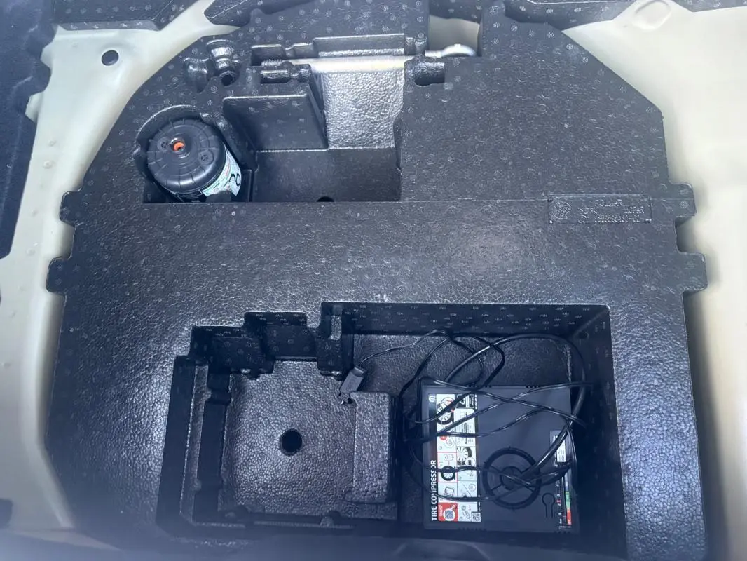 Rangement sous le coffre d'une Citroën C3 gris foncé 2025, montrant le compresseur de pneu et espace de rangement en mousse noire.