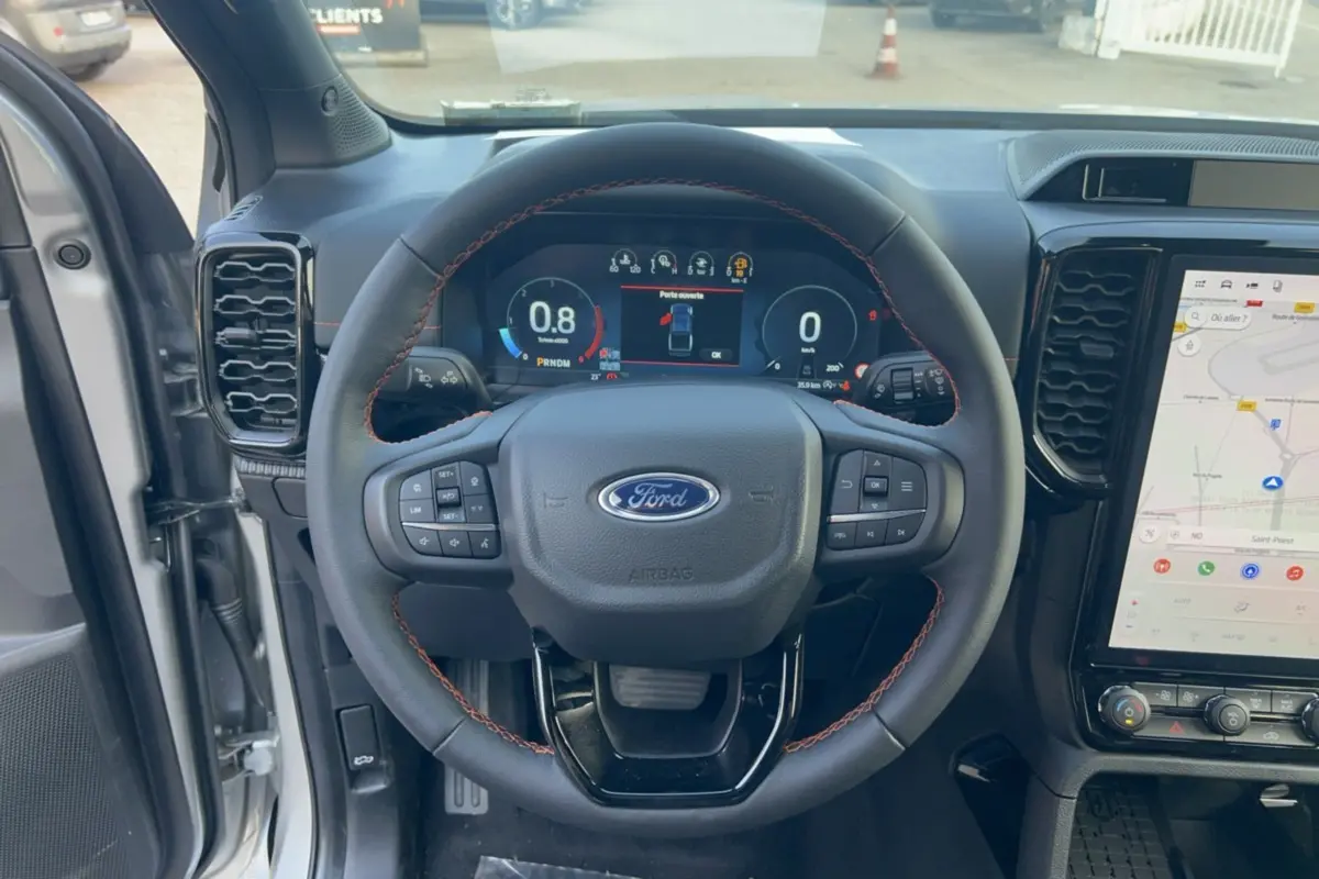 Vue centrée sur le volant noir avec coutures rouges du Ford Ranger Wildtrak 2026, tableau de bord digital et écran tactile GPS visible.