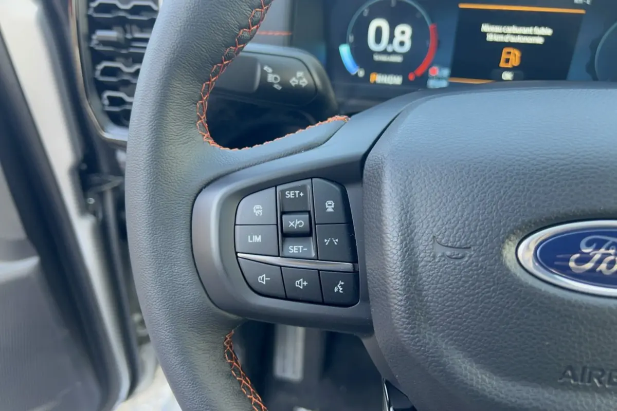 Gros plan sur le volant cuir noir avec surpiqûres orange du Ford Ranger Wildtrak 2026, boutons multifonctions visibles.