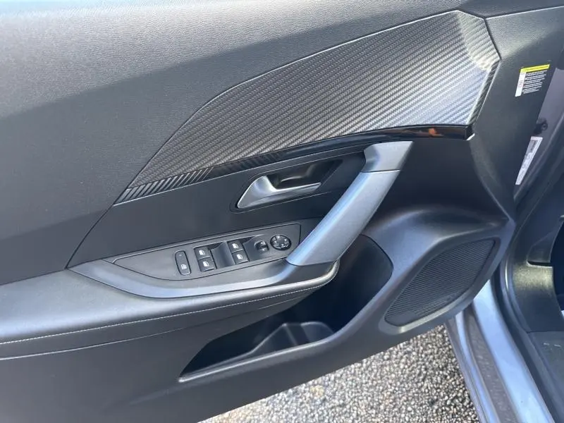 Vue rapprochée de la porte avant gauche du Peugeot 2008 gris Artense avec commandes de vitres et insert effet carbone.