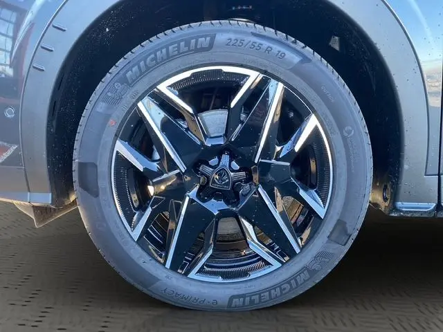 Gros plan sur la roue avant droite du Peugeot 5008 Hybrid gris titane, mettant en valeur la jante noire et brillante avec pneus Michelin.