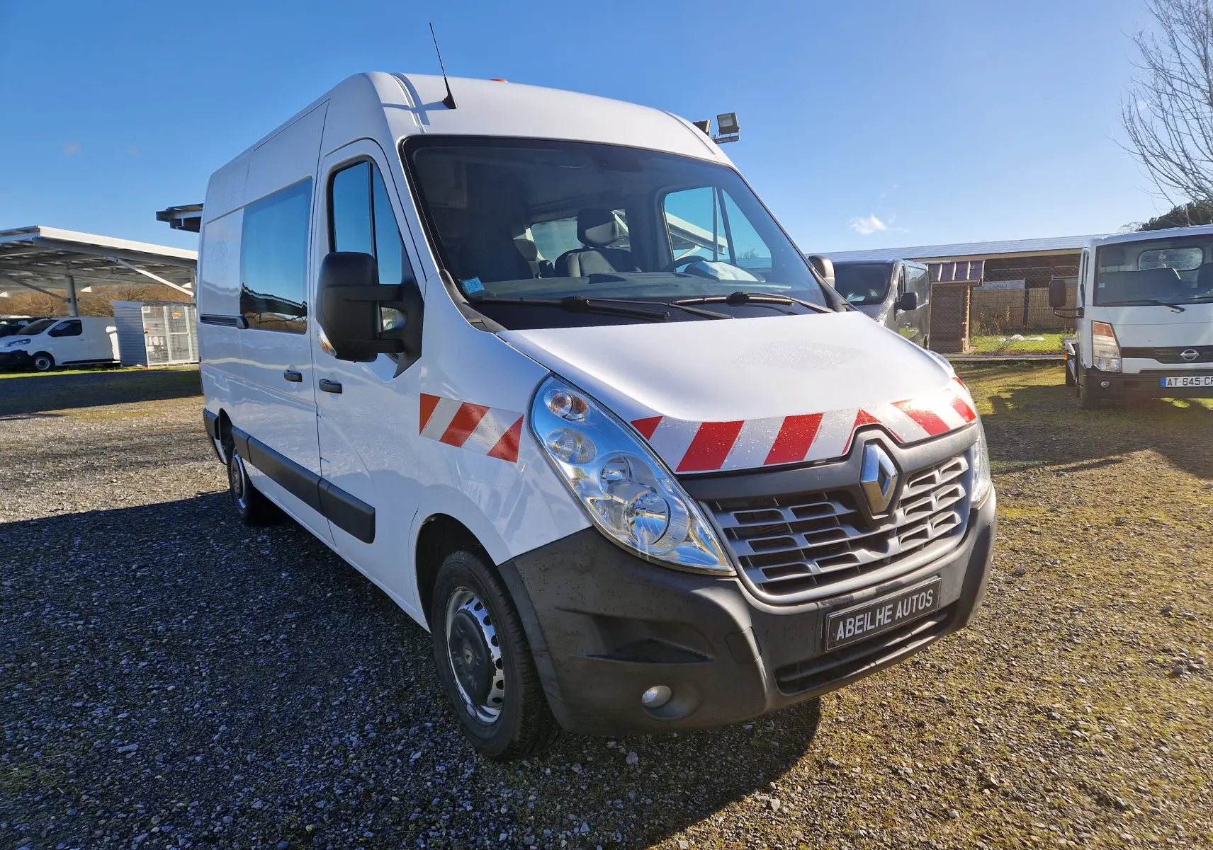 Renault Master cabine approfondie blanc vu en 3/4 avant droit avec bandes rouges et blanches sur la calandre et l'aile.